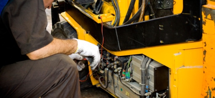 A technician checking some wiring on a yellow forklift